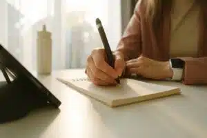 Close-up of a woman’s hand taking notes with a pen while using a tablet, illustrating professional interpreting services in action.