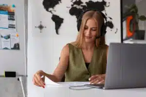Video interpreter blonde woman wearing headphones and working at a computer to deliver real time multilingual communication online.