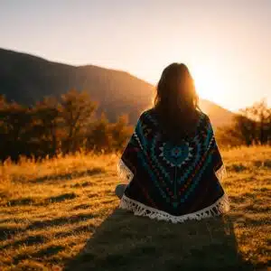 Woman in a traditional blanket sitting on a hillside at sunset representing indigenous translation, cultural preservation, and language diversity.
